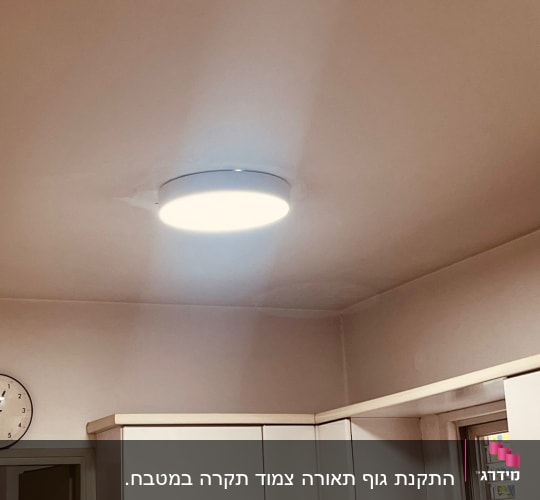מנורה עגולה מותקנת בתקרה מעל ארונות מטבח לבנים